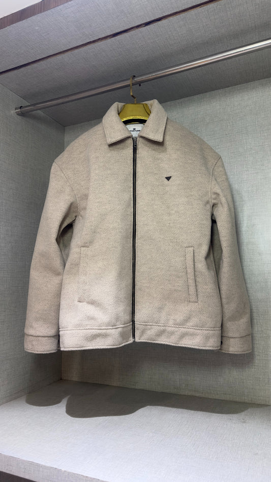 The full-front view of a cream-colored tweed jacket displayed in a wardrobe niche, its boxy shoulders and straight-cut sleeves fully visible. The jacket’s structured silhouette casts a soft shadow across the bottom shelf, highlighting the contrast between its textured surface and the smooth fabric lining of the closet.