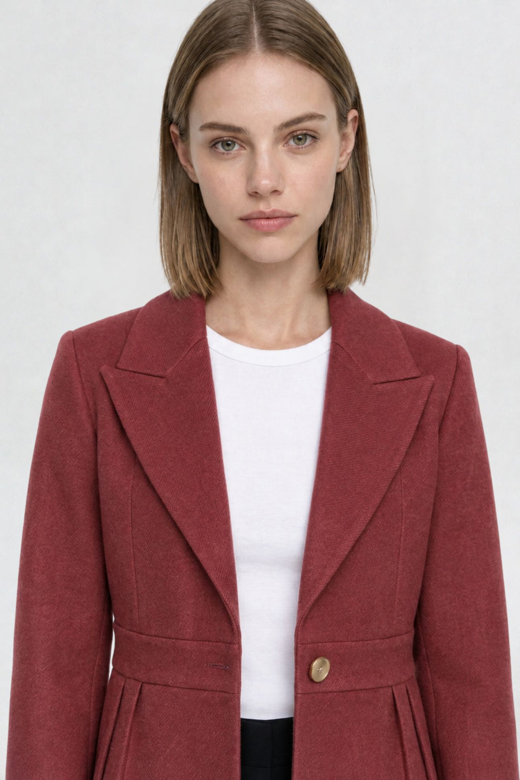 Close-up of copper red short blazer coat, peaked lapel and gold button detail on textured herringbone-weave fabric