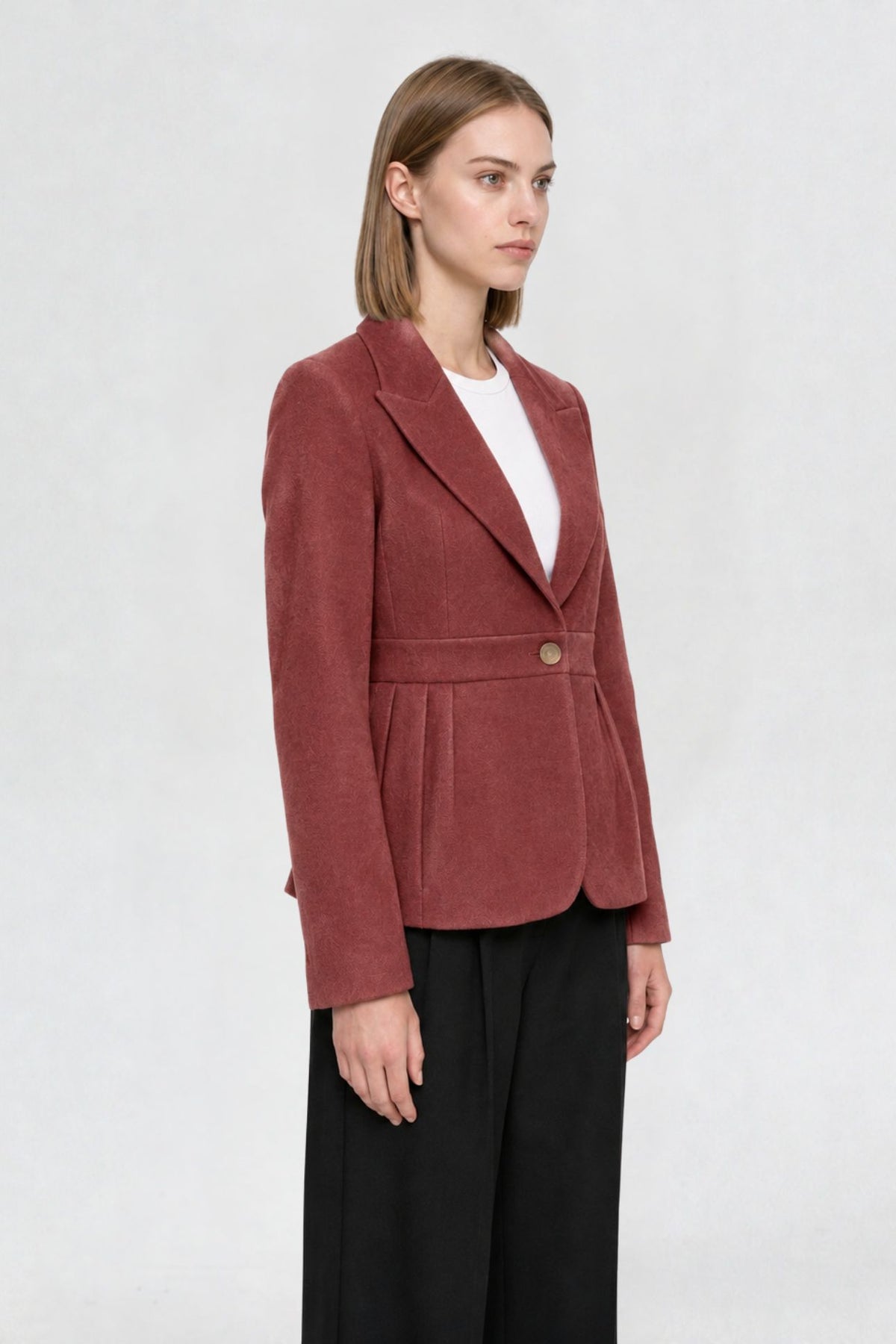 Side view of copper red short blazer coat showing peaked lapel, single gold button, and pleated waist seam