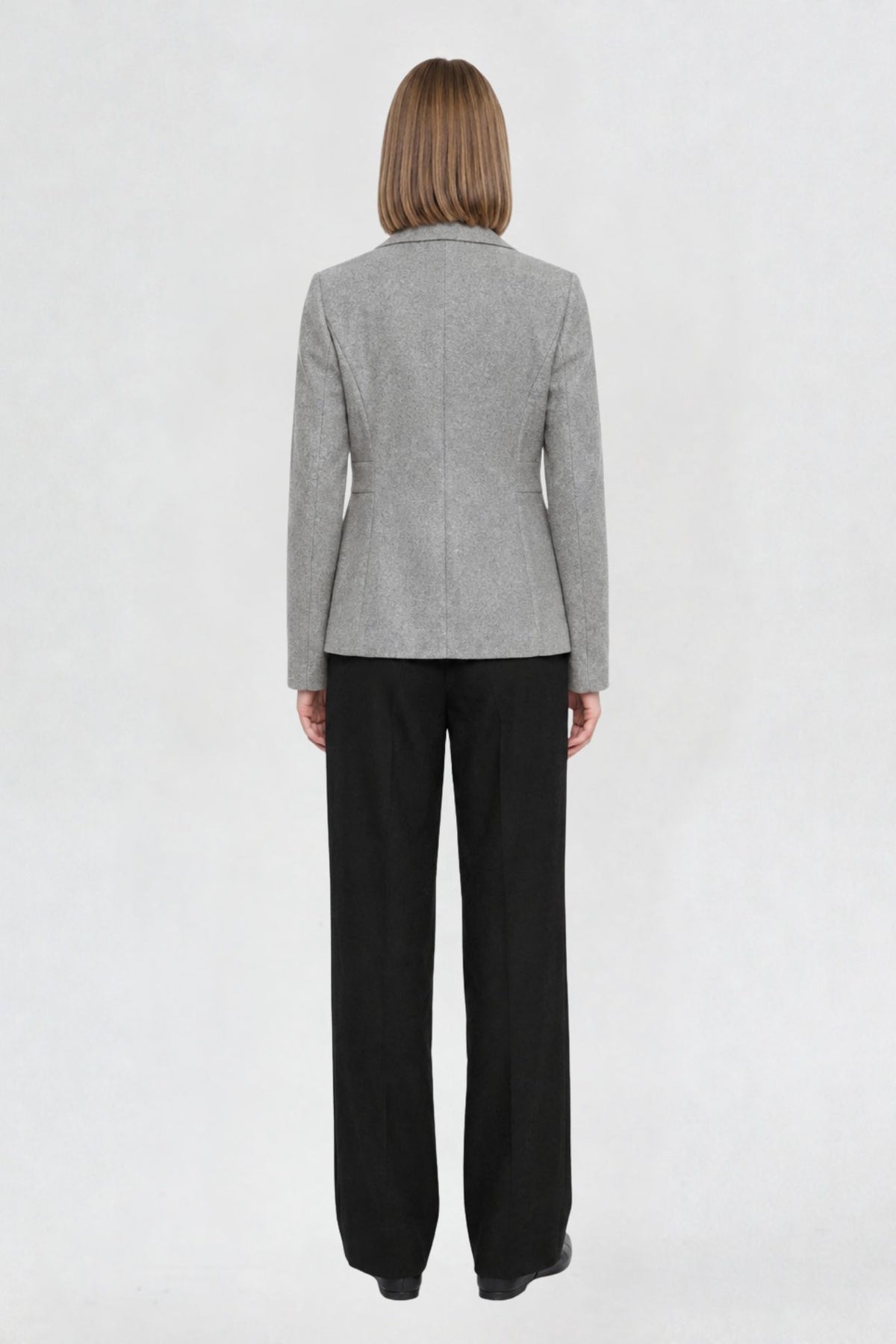 Back view of grey short blazer coat showing tailored back seams and welt pocket detail
