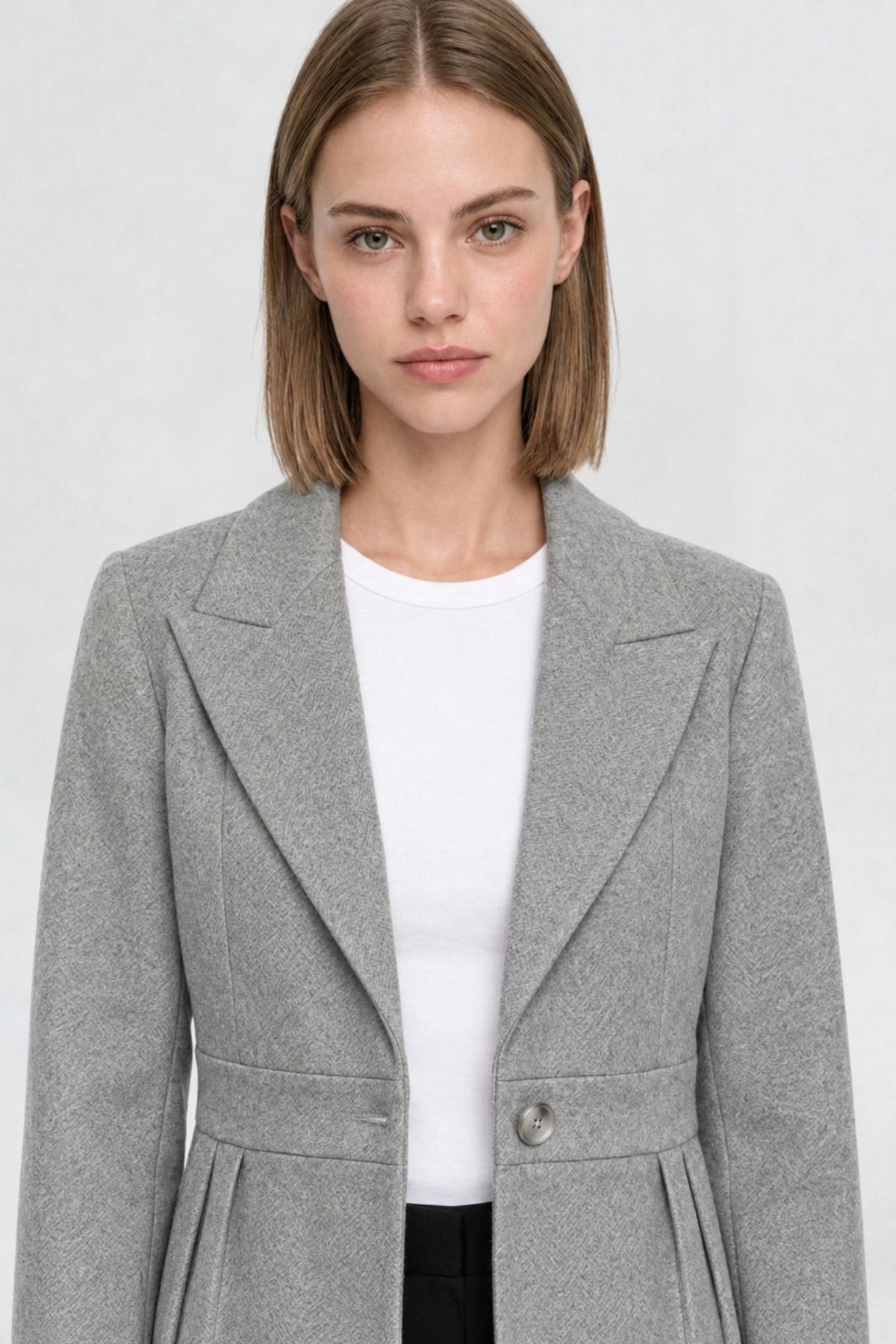 Close-up of grey short blazer coat, peaked lapel and gold button detail on textured herringbone-weave fabric