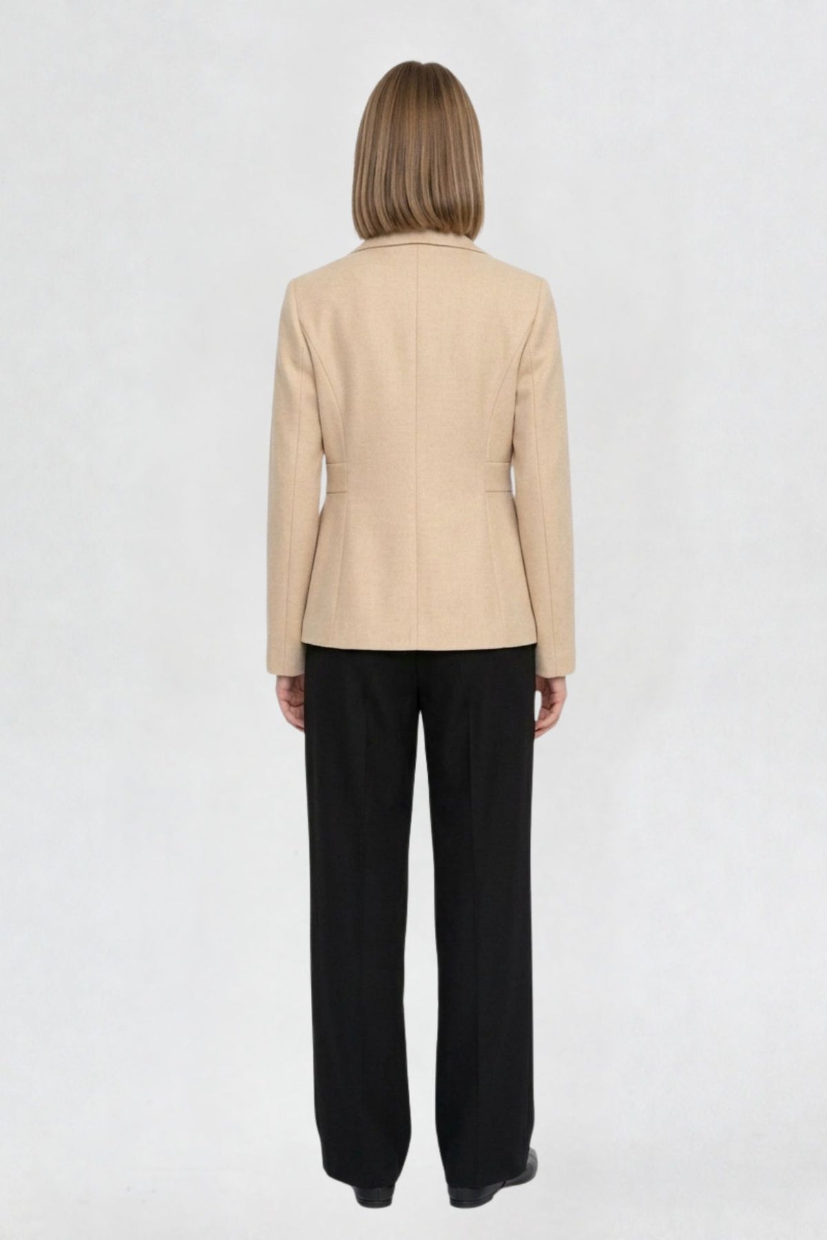 Back view of light beige short blazer coat showing tailored back seams and welt pocket detail
