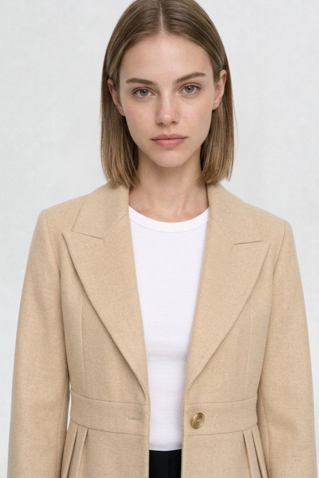 Close-up of light beige short blazer coat, peaked lapel and gold button detail on textured herringbone-weave fabric