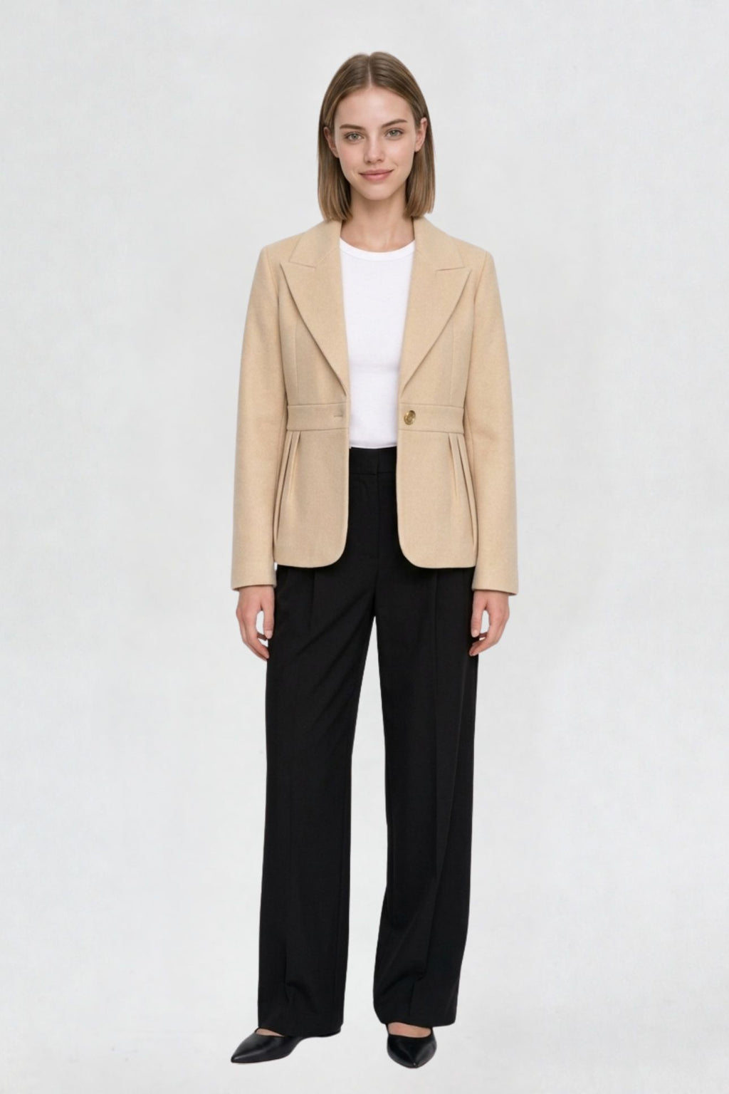 Women's light beige short blazer coat, full front view, single-button closure, pleated peplum hem, styled with black wide-leg trousers