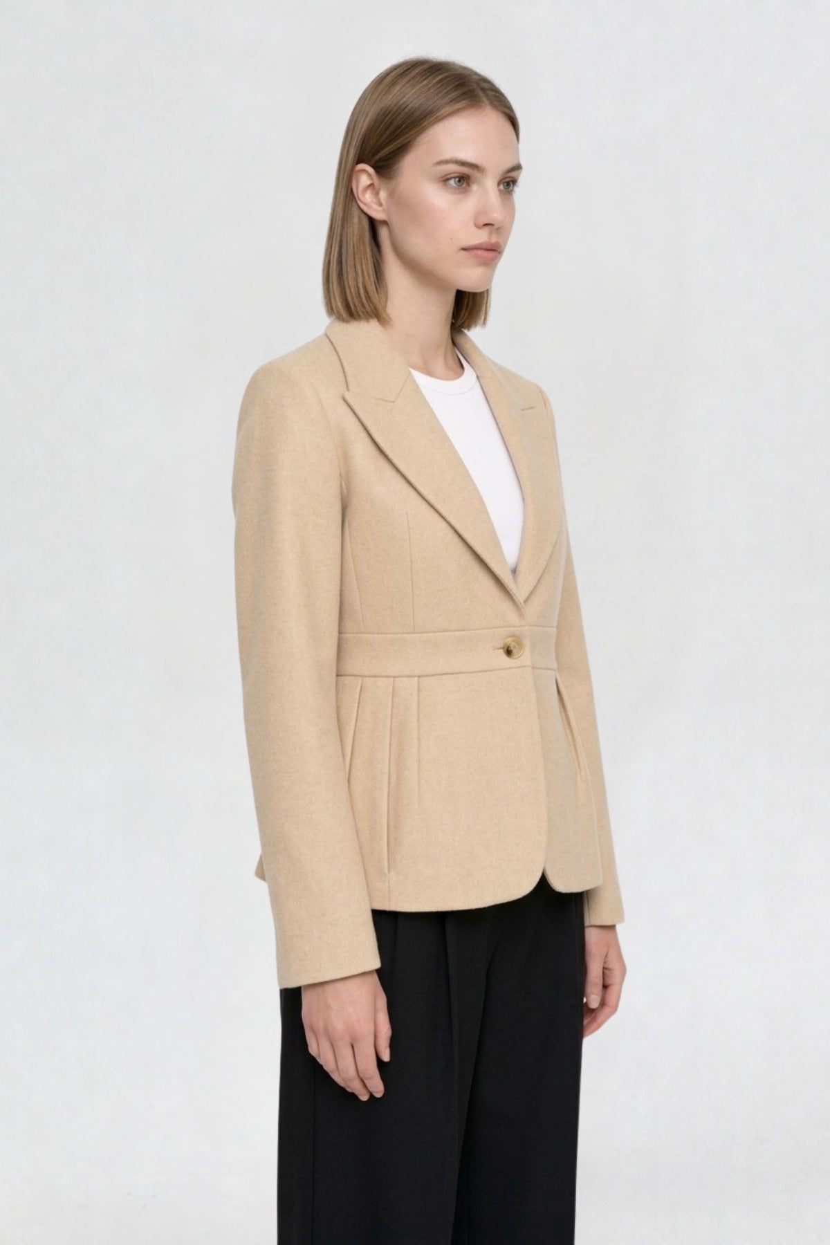 Side view of light beige short blazer coat showing peaked lapel, single gold button, and pleated waist seam