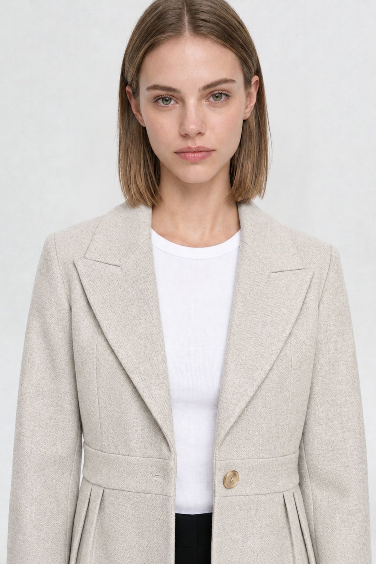 Close-up of off white short blazer coat, peaked lapel and gold button detail on textured herringbone-weave fabric