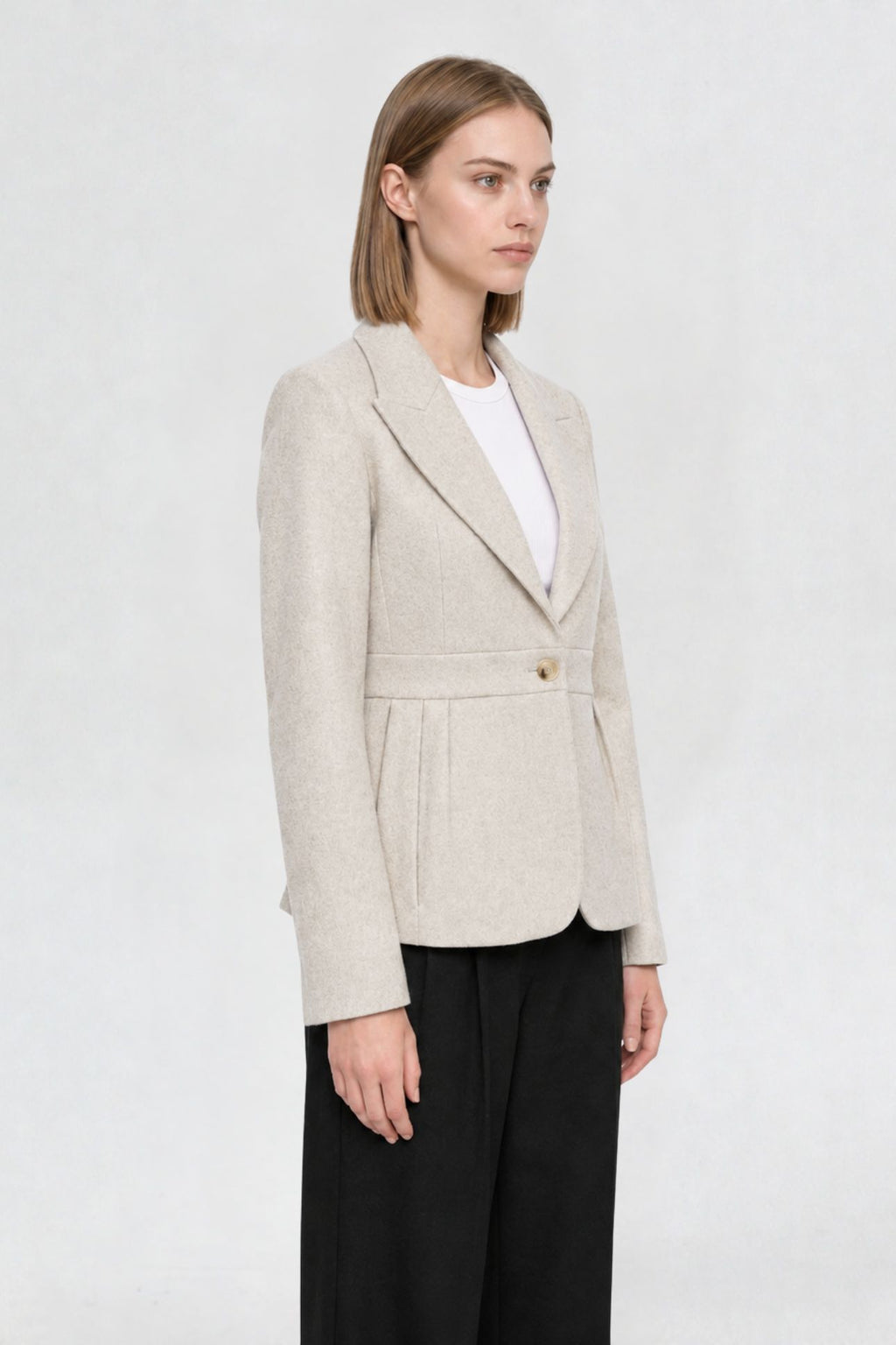 Side view of off white short blazer coat showing peaked lapel, single gold button, and pleated waist seam