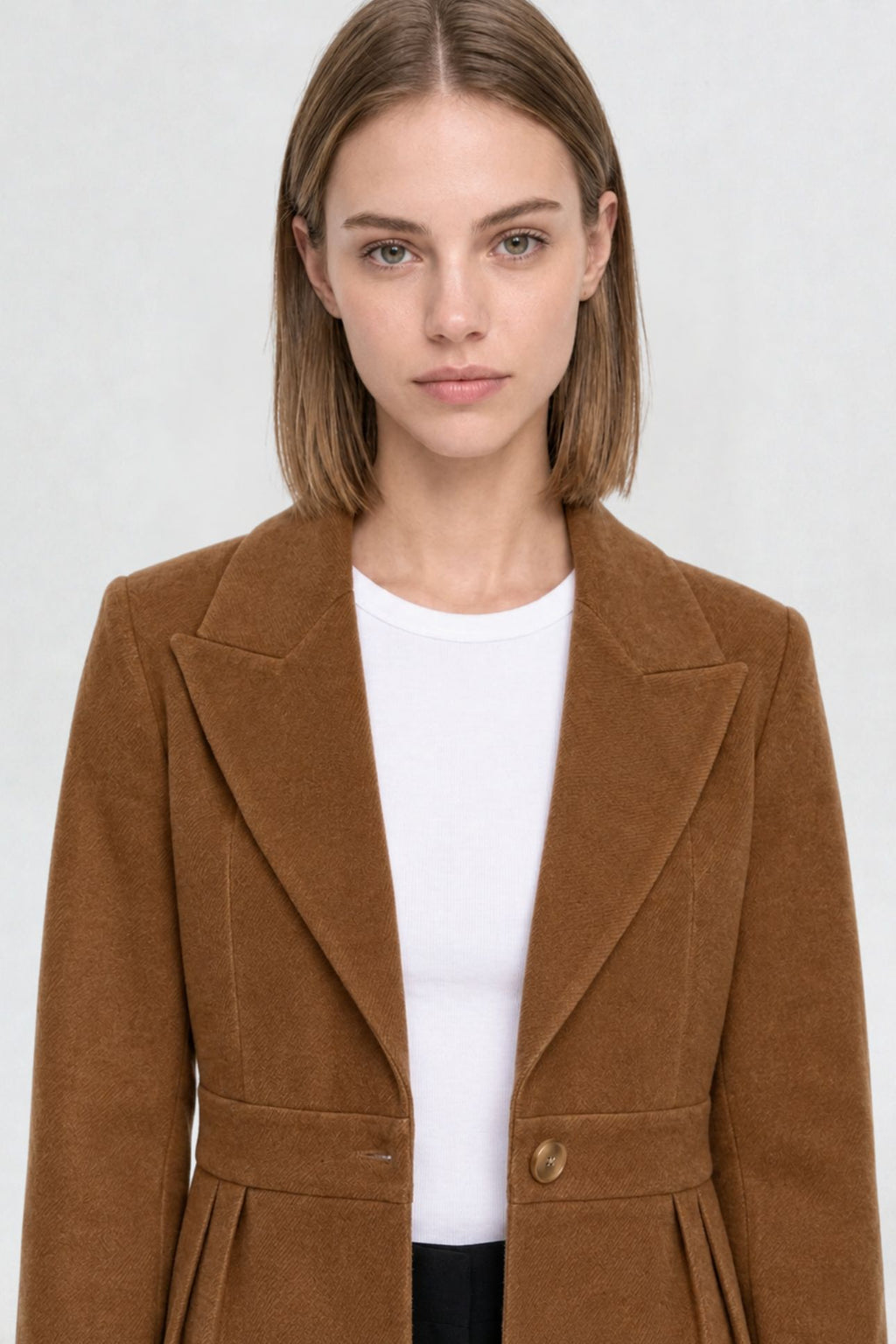 Close-up of tan brown short blazer coat, peaked lapel and gold button detail on textured herringbone-weave fabric