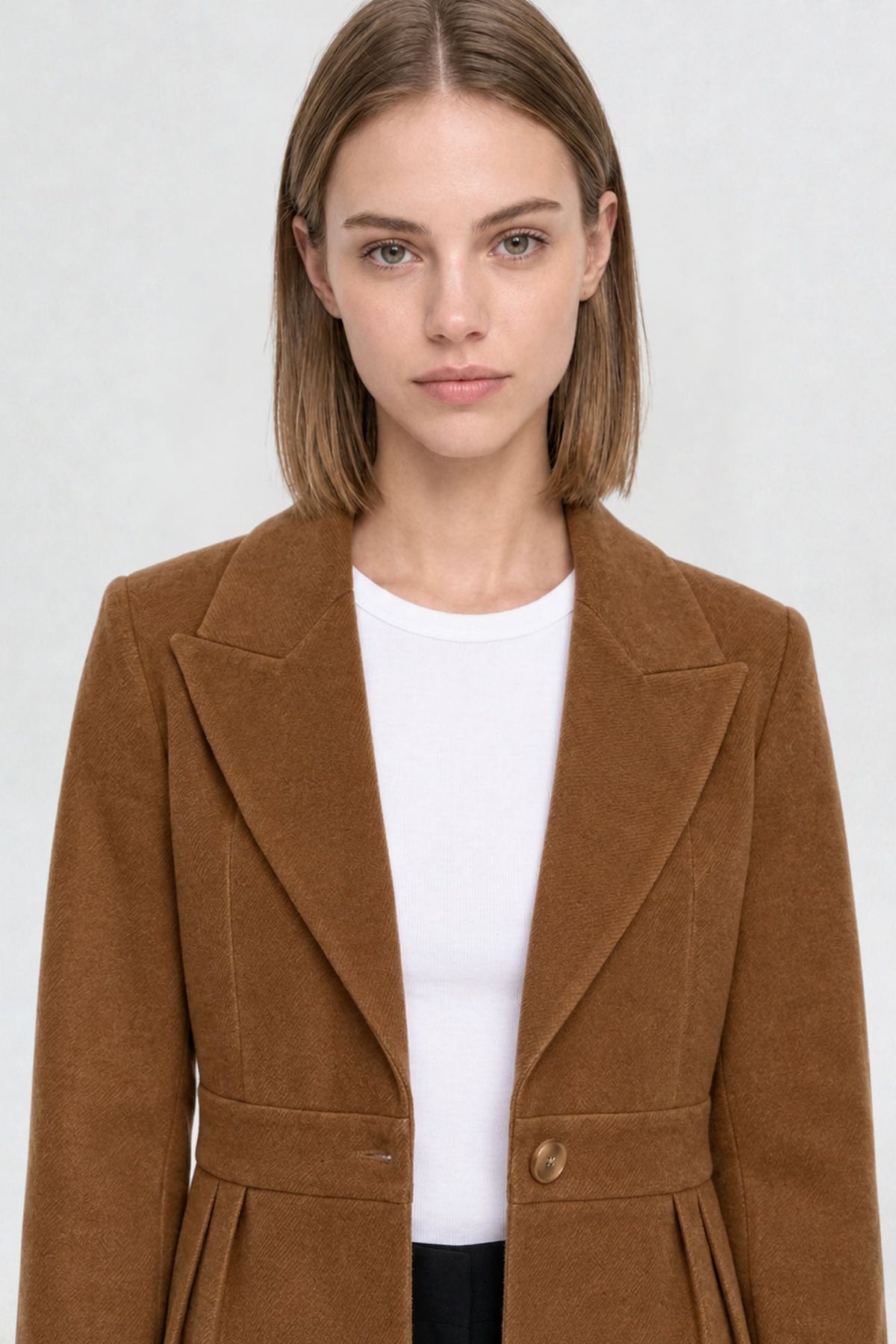 Close-up of tan brown short blazer coat, peaked lapel and gold button detail on textured herringbone-weave fabric