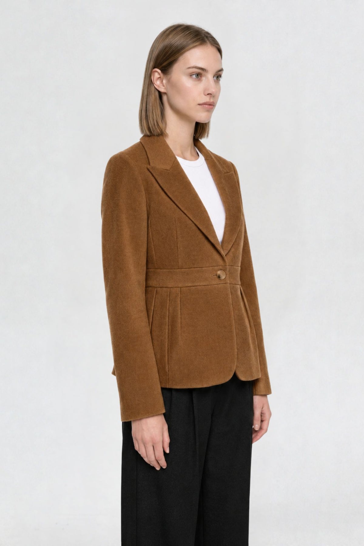 Side view of tan brown short blazer coat showing peaked lapel, single gold button, and pleated waist seam