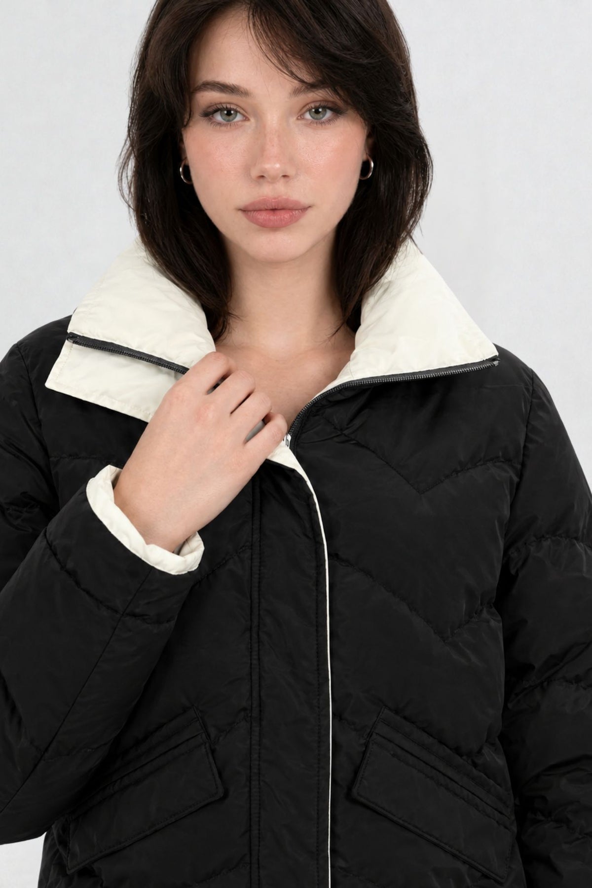 Close-up of black puffer jacket showing cream contrast zip trim, chevron quilting, and collar detail