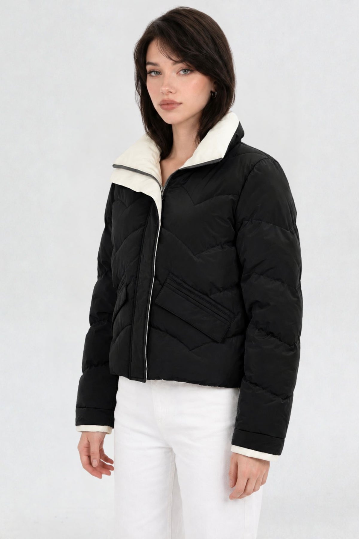 Side view of black puffer jacket showing cream contrast collar and flap pocket detail