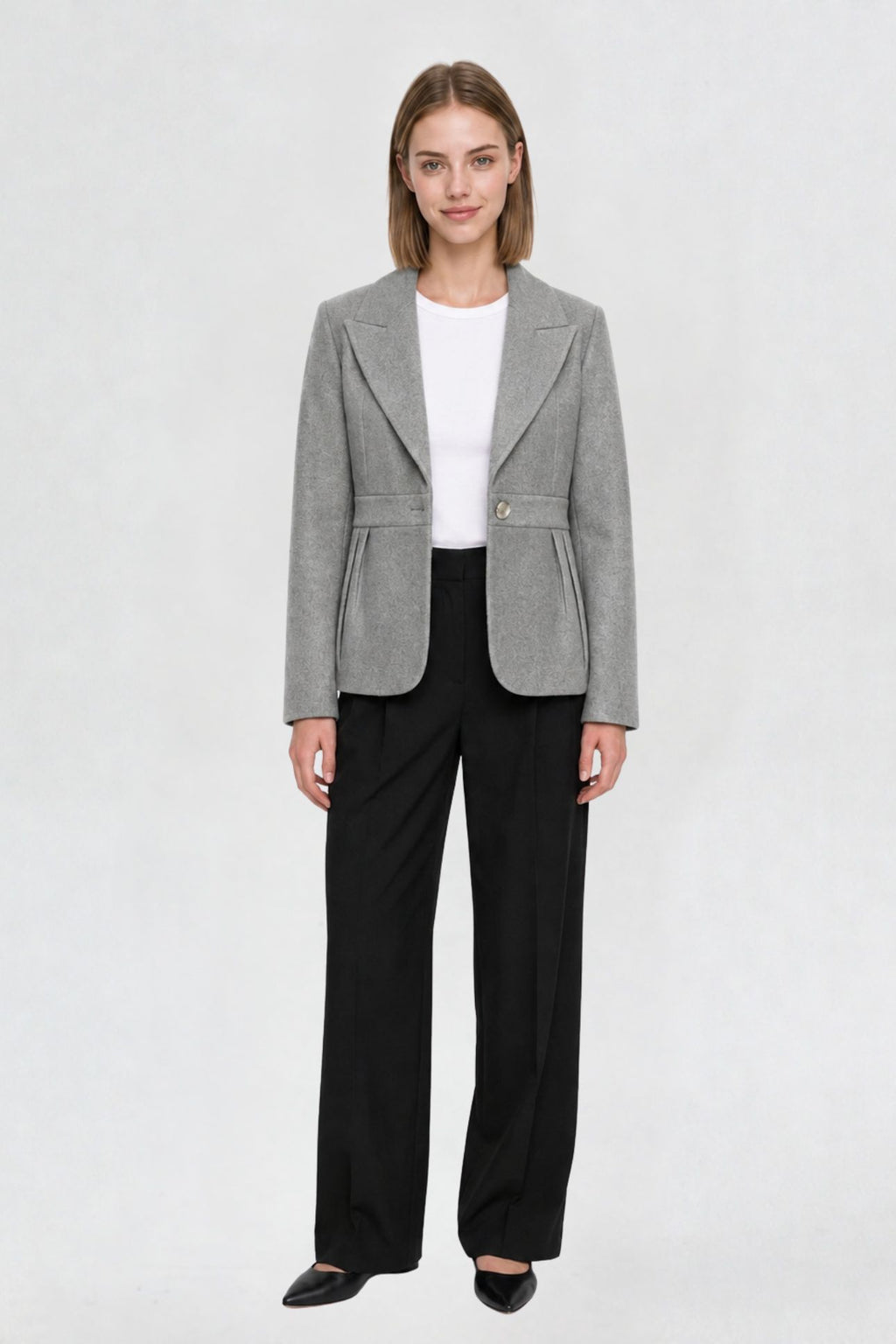 Women's grey short blazer coat, full front view, single-button closure, pleated peplum hem, styled with black wide-leg trousers