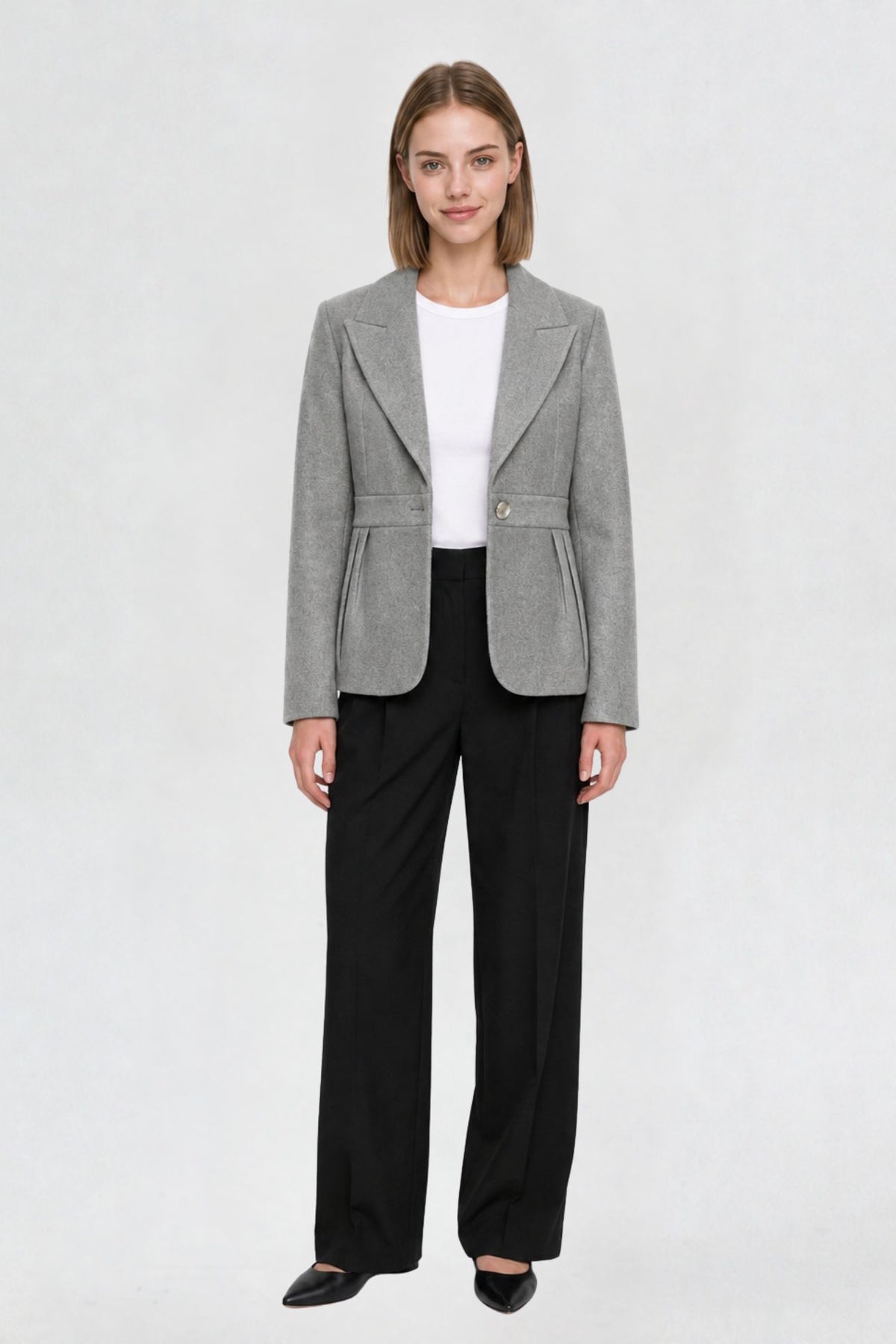 Women's grey short blazer coat, full front view, single-button closure, pleated peplum hem, styled with black wide-leg trousers